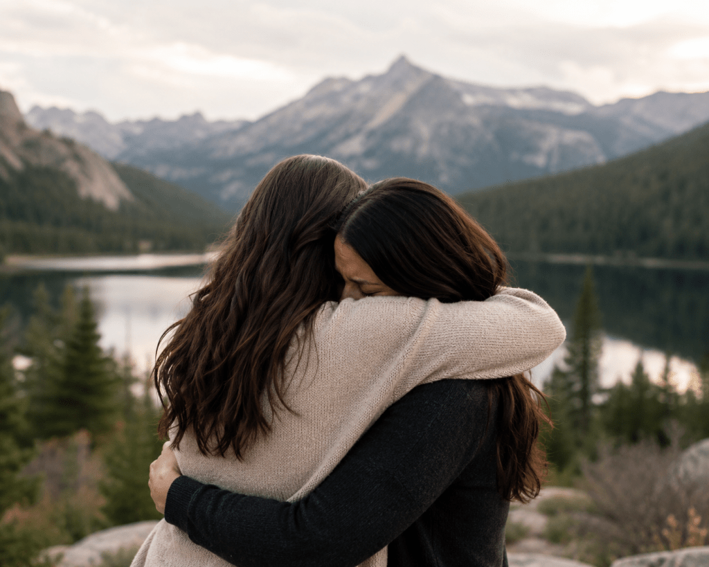 Two women hugging next to a lake and mountains